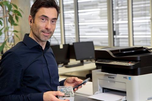 Siegbert Versümer mit Smartphone und Tonaufzeichnungsgerät vor einem Drucker